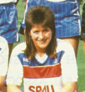 Smiling woman with brown shoulder-length hair in a white t-shirt with blue and red stripes