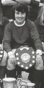A smiling woman with short dark hair sitting down and holding a trophy shield